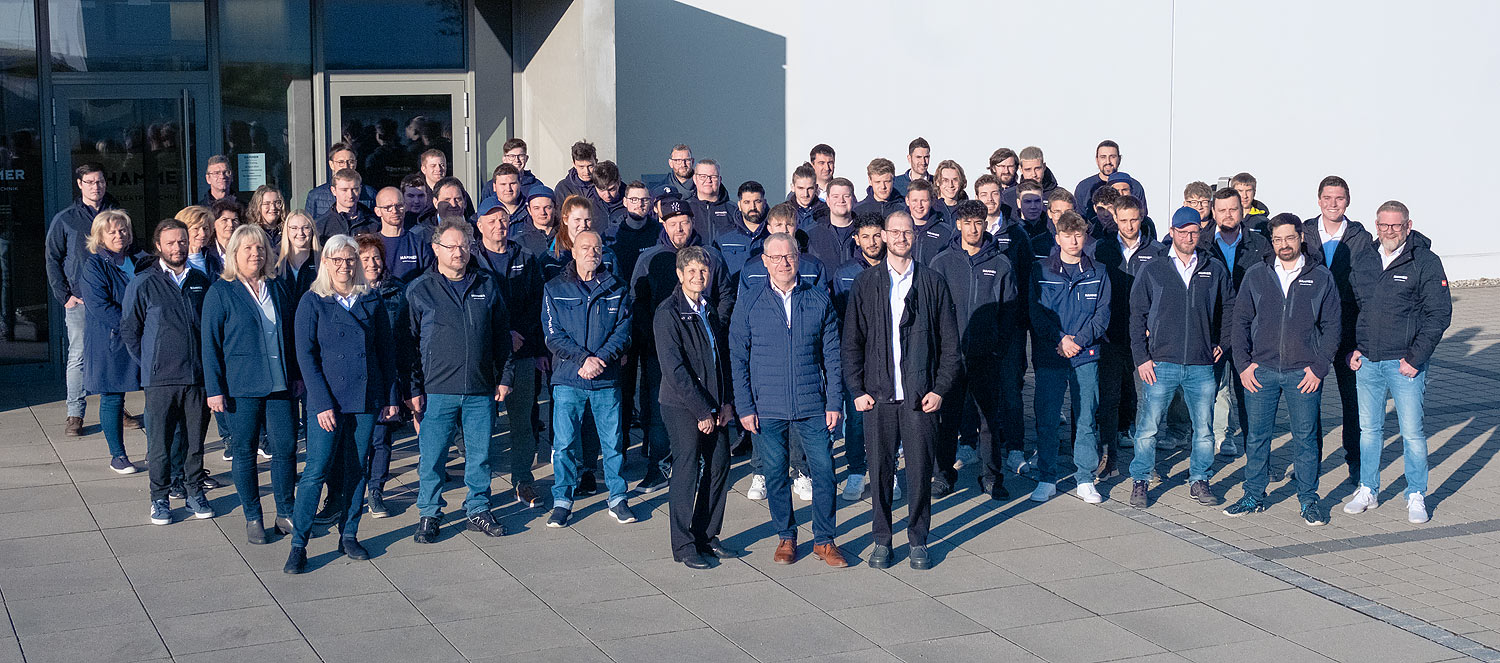 Eine große Gruppe von etwa 60 Männern und Frauen posiert für ein Gruppenfoto im Freien vor dem Firmengebäude von HAMMER Elektrotechnik.